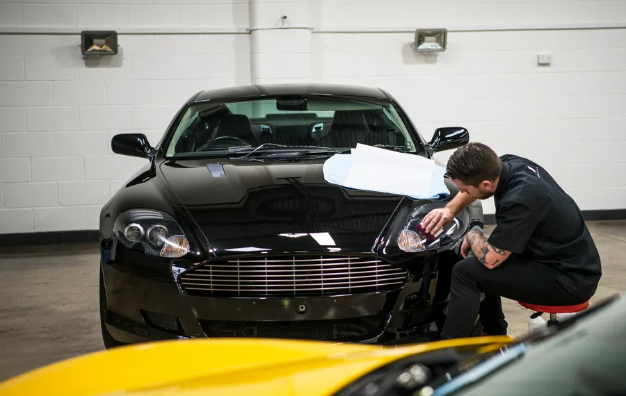 Protection film being fitted to the headlight of a black Aston Martin DB9
